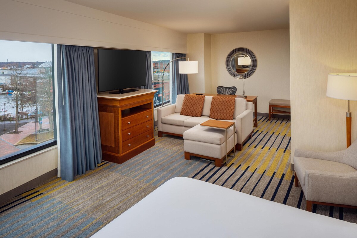 A hotel room with a large bed, a sofa, a TV, a dresser, and a view of the city.