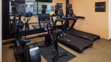 Un gimnasio con cintas de correr, elípticas y un espejo grande.
