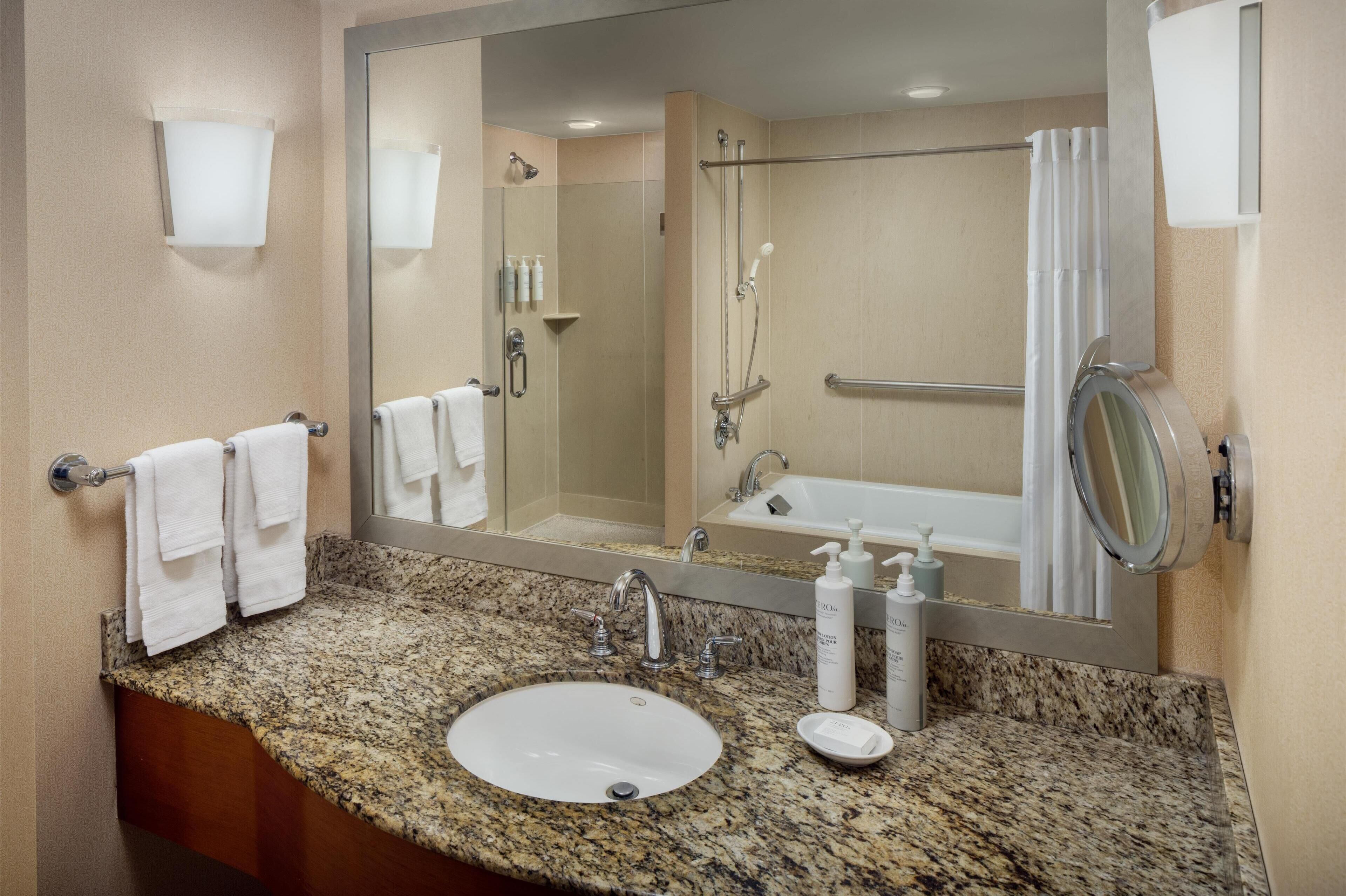 Une salle de bain avec un lavabo surmonté d’un plan en granit, un miroir, un porte-serviettes, une douche avec une porte en verre et une baignoire.
