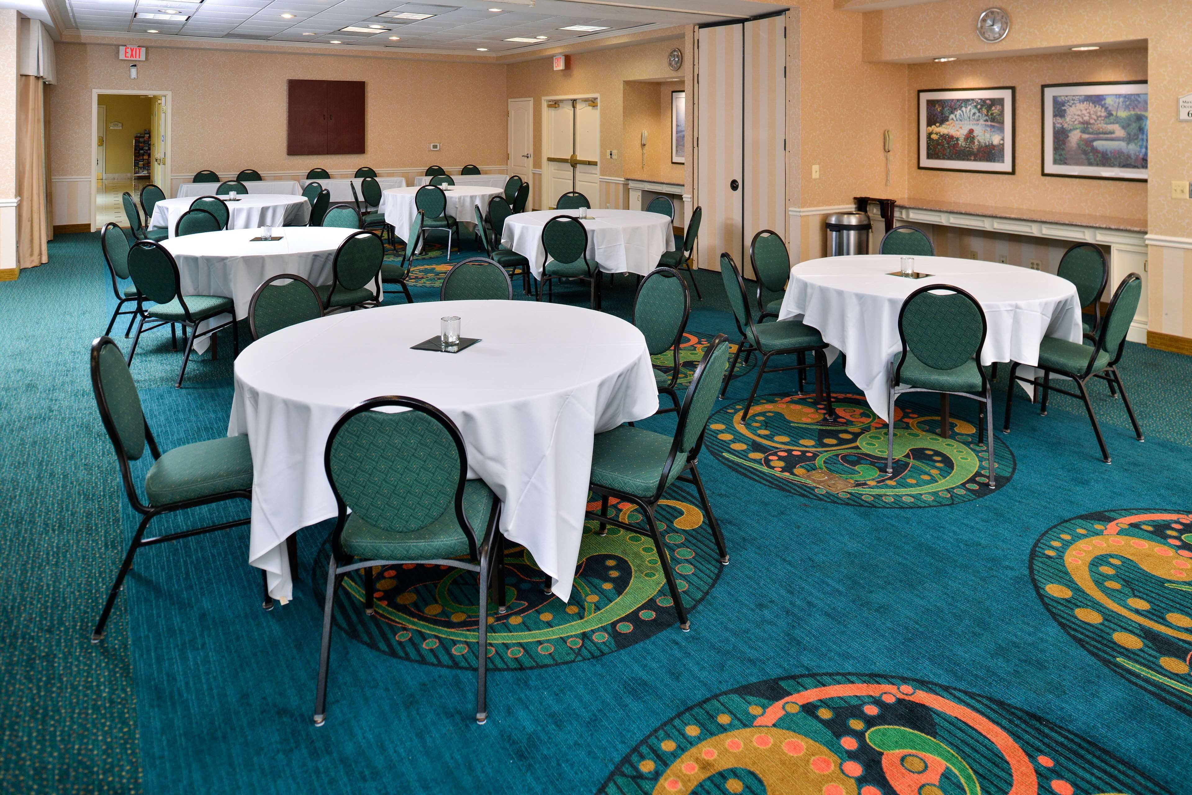 A conference room with multiple round tables and chairs, carpeted floor, and a door leading to another room.