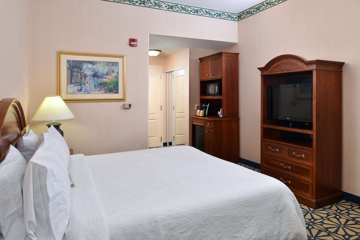 A hotel room with a bed, a television, a wooden cabinet, and a painting on the wall.