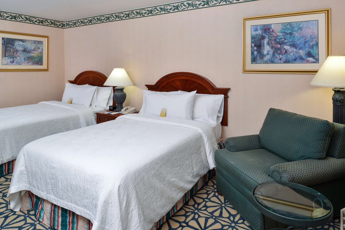 A hotel room with two single beds, a green sofa, a glass coffee table, and two paintings on the walls.