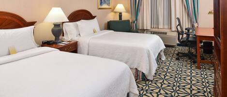 A hotel room with two beds, a desk, a chair, and a patterned floor.