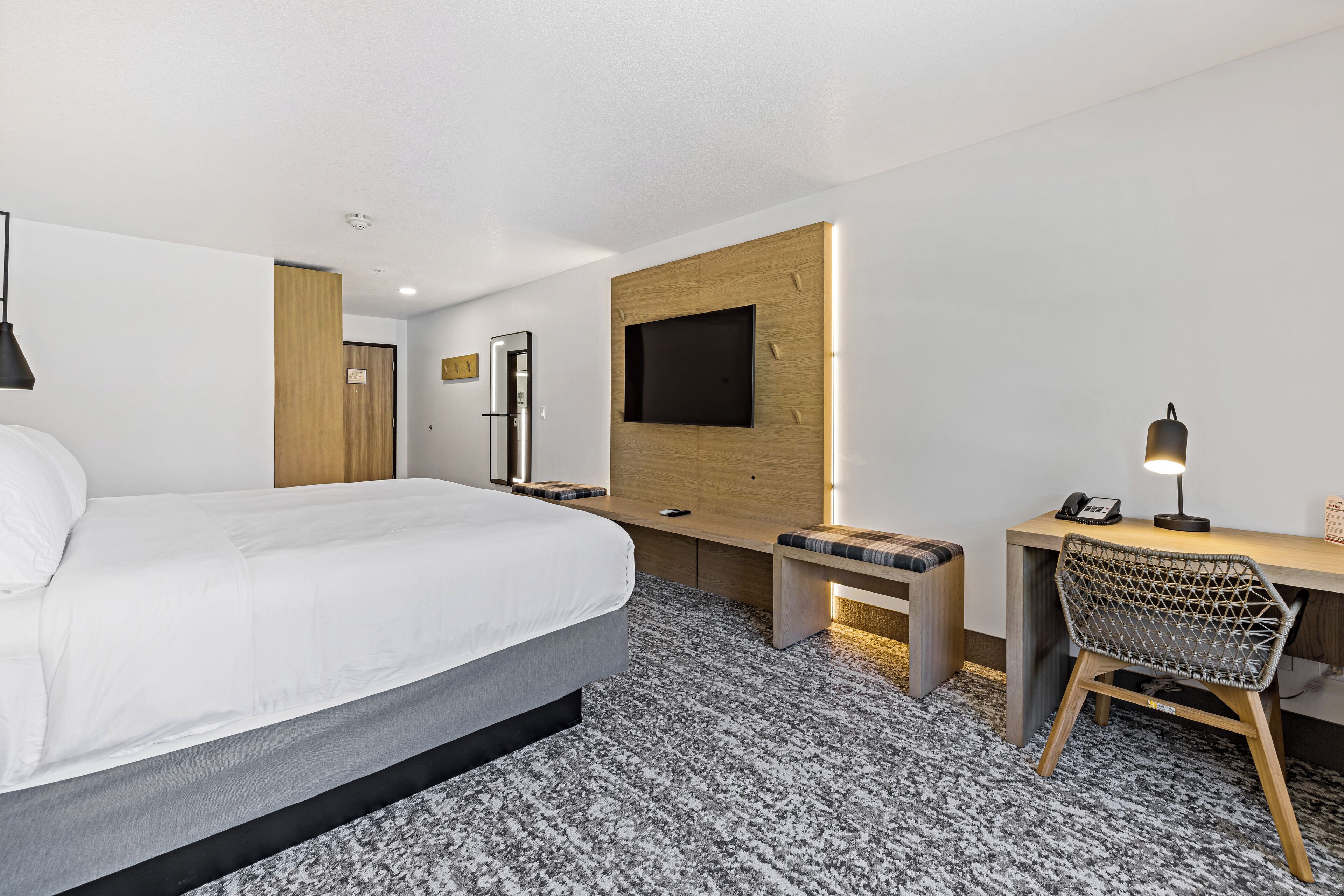 Una habitación de hotel moderna con una cama grande, un escritorio con una silla, un televisor montado en la pared y una pequeña zona de estar.