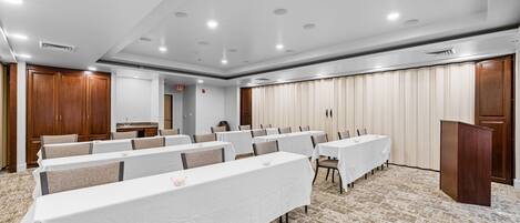 Un salón de conferencias con filas de mesas, un atril y piso alfombrado.