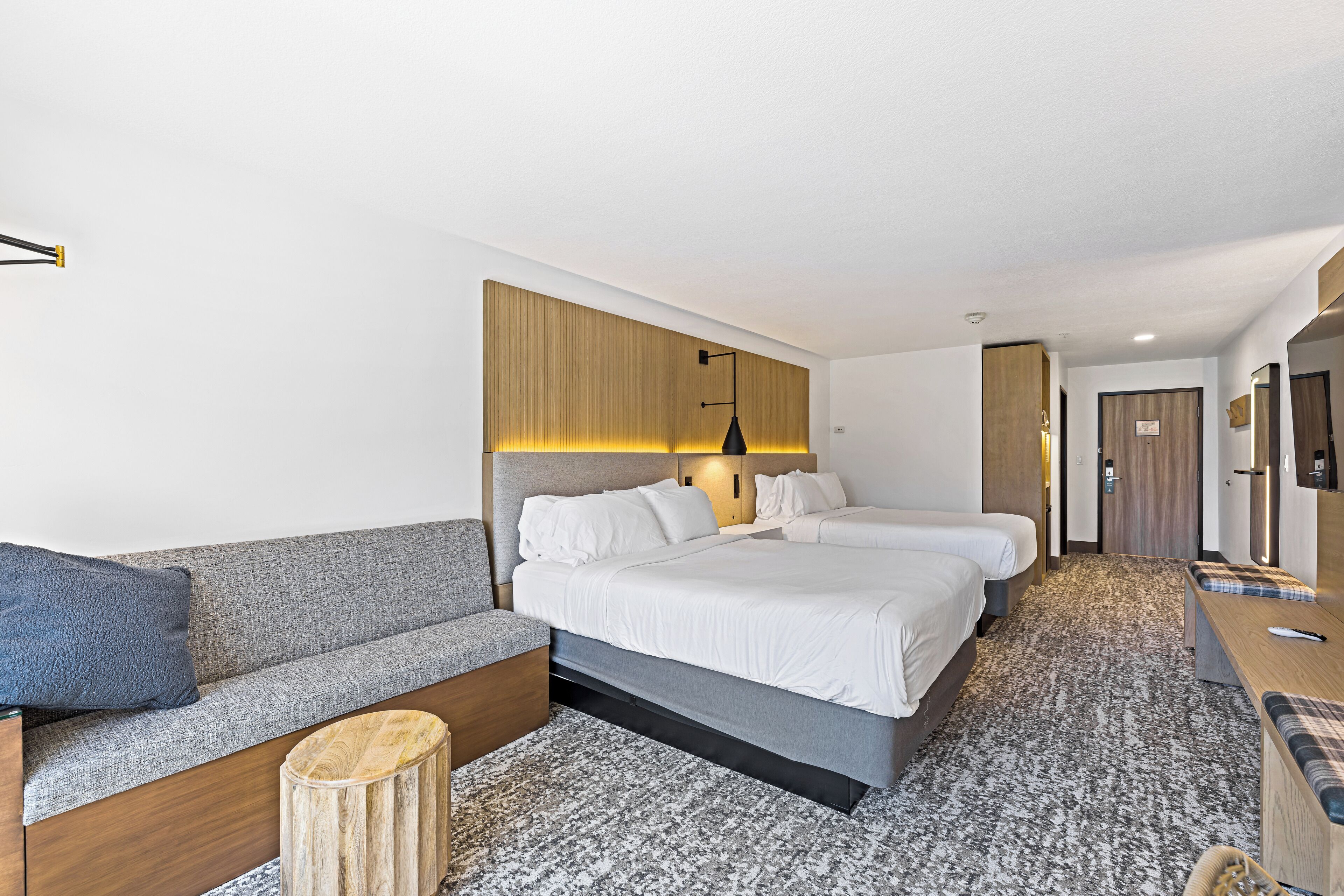 A hotel room with two beds, a sofa, a small wooden stool, and a desk with a chair.