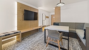 A modern living room with a flat-screen TV, wooden paneling, a sofa, a dining table, and a patterned rug. - The Evergreen Hotel (McCall)