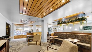 A modern cafe with wooden ceiling beams, cushioned seating, and hanging plants. - The Evergreen Hotel (McCall)