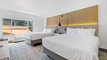 A modern hotel room with two beds, a large window, and a view of the outdoors.