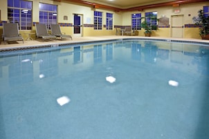 Una piscina interior con sillones de descanso, una planta en maceta y carteles con las normas de la piscina.