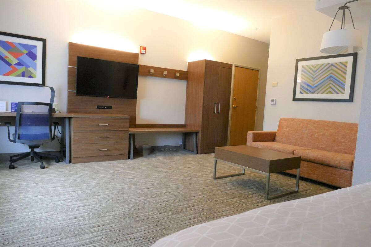 A hotel room with a desk, chair, television, wardrobe, sofa, and a bed.