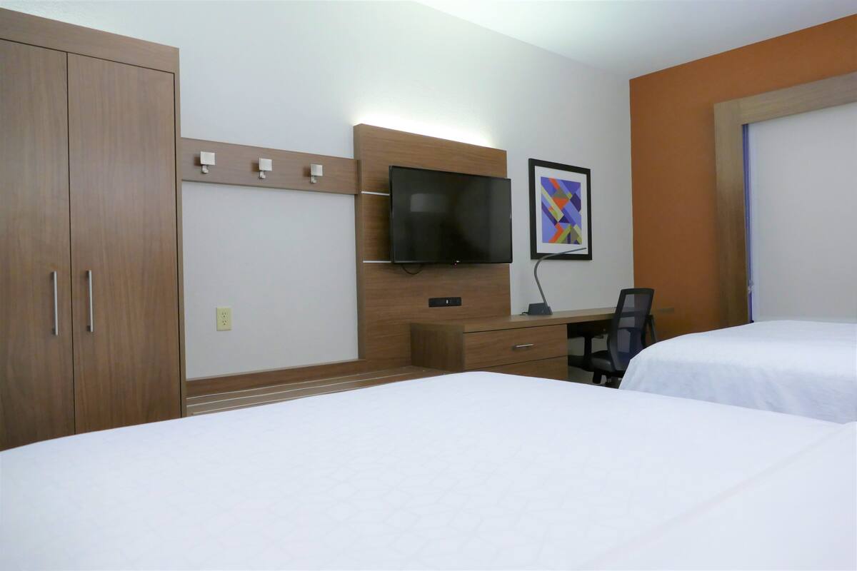 A hotel room with two beds, a desk with a chair, a TV mounted on the wall, and a framed picture.