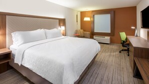 A hotel room with a large bed, a desk, a chair, a TV, and a wall-mounted air conditioner.