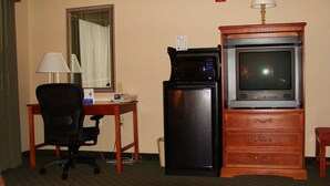 A hotel room with a desk, a chair, a microwave, a refrigerator, a television, and a dresser.