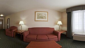 A hotel room with a red sofa, two armchairs, a coffee table, two bedside lamps, a framed picture on the wall, and a large window with curtains.