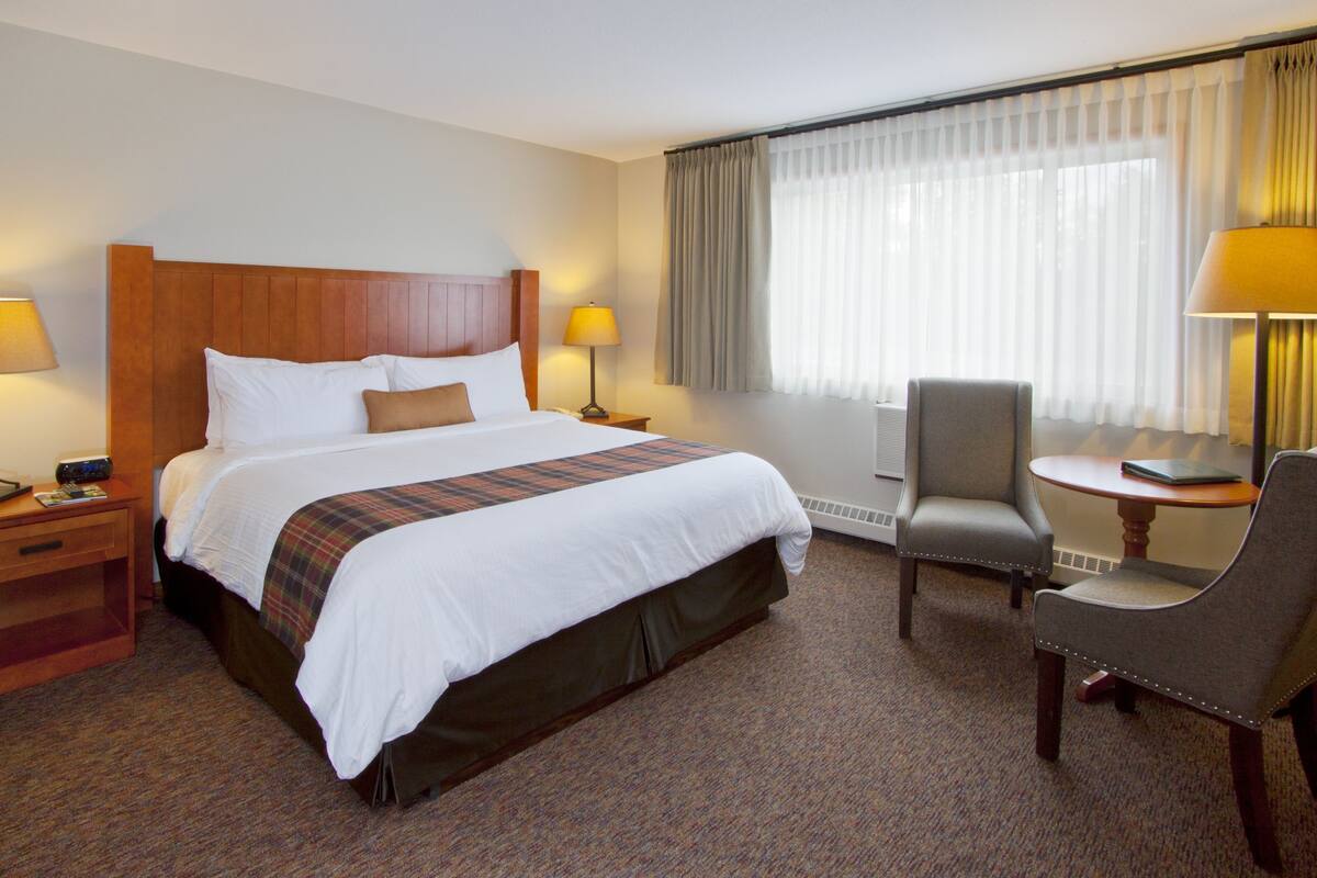 A hotel room with a large bed, two bedside tables with lamps, a chair, and a window with curtains.