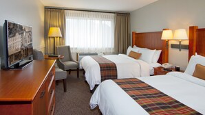 A hotel room with two beds, a desk, a chair, a television, and a window with curtains.
