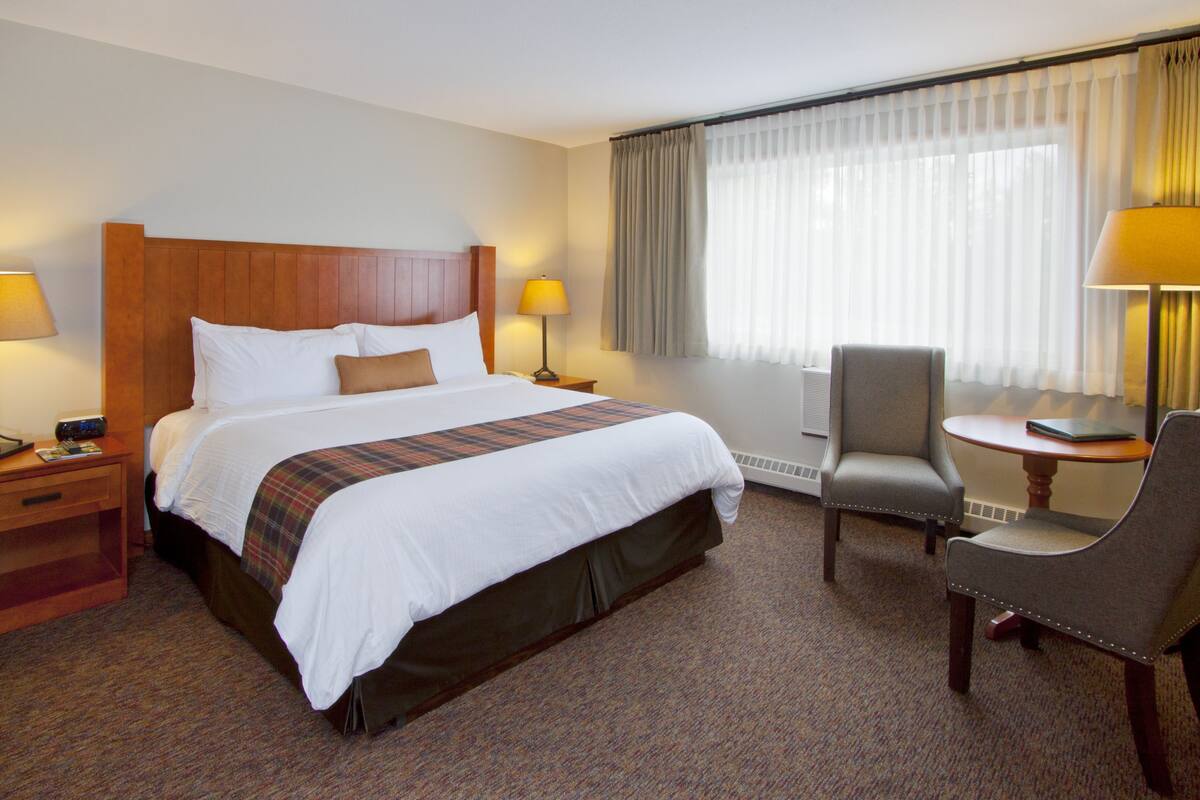 A hotel room with a large bed, two bedside tables with lamps, a chair, and a window with curtains.