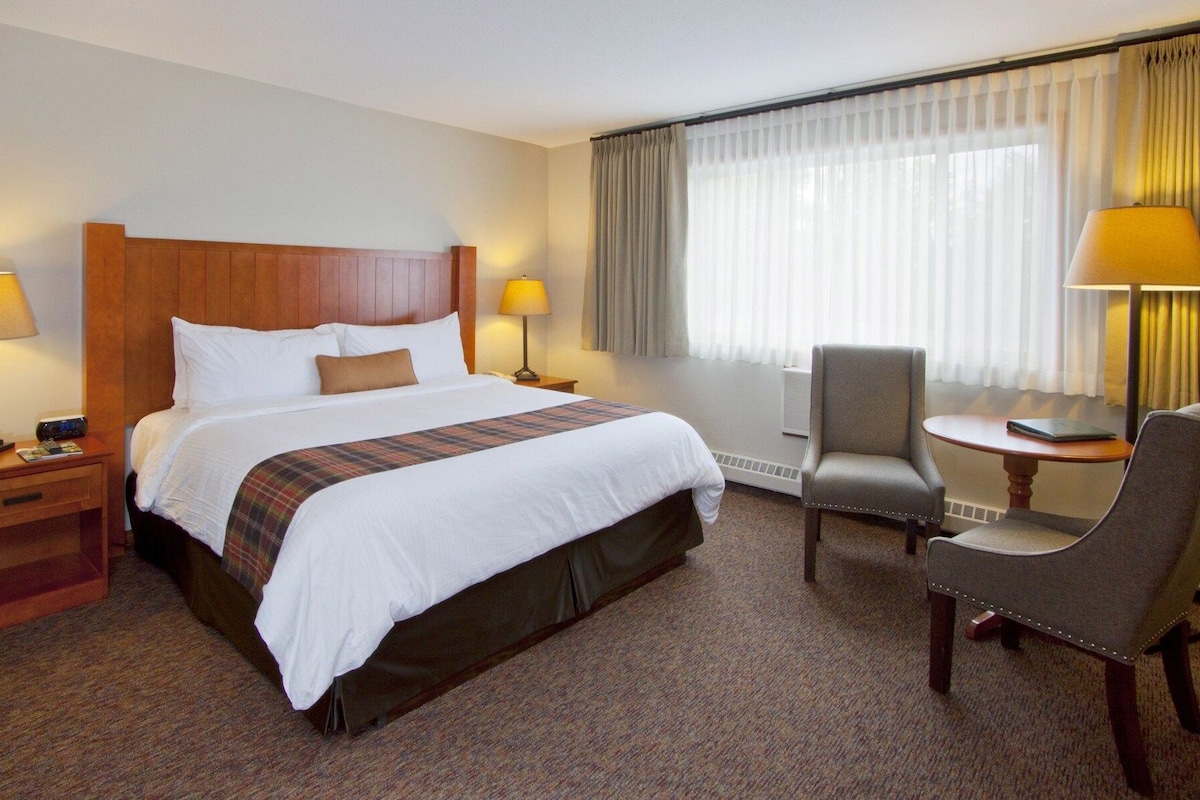 A hotel room with a large bed, two bedside tables with lamps, a chair, and a window with curtains.