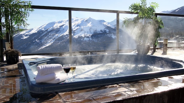A hot tub with towels and glasses, surrounded by potted plants, overlooking a snowy mountain range.