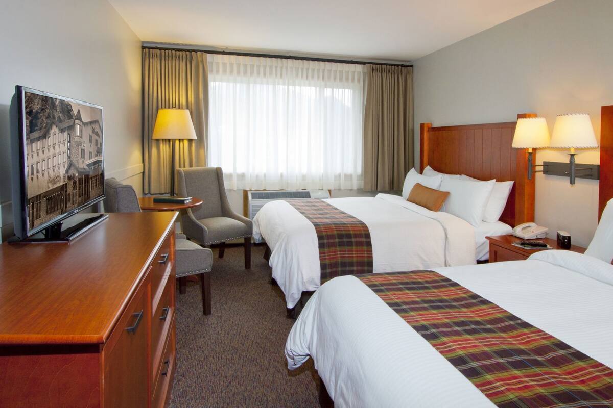 A hotel room with two beds, a desk, a chair, a TV, and a window with curtains.