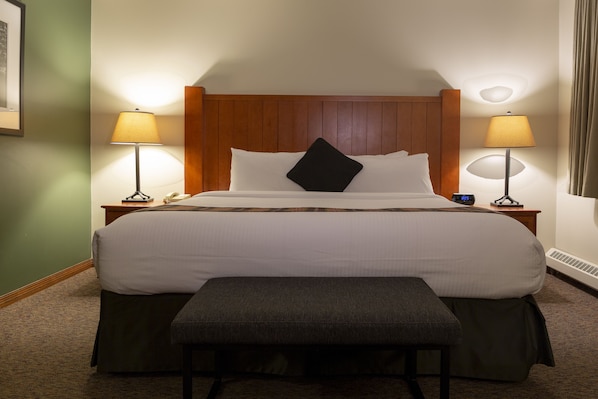 A hotel room with a large bed, two bedside tables with lamps, a bench, and a framed picture on the wall.