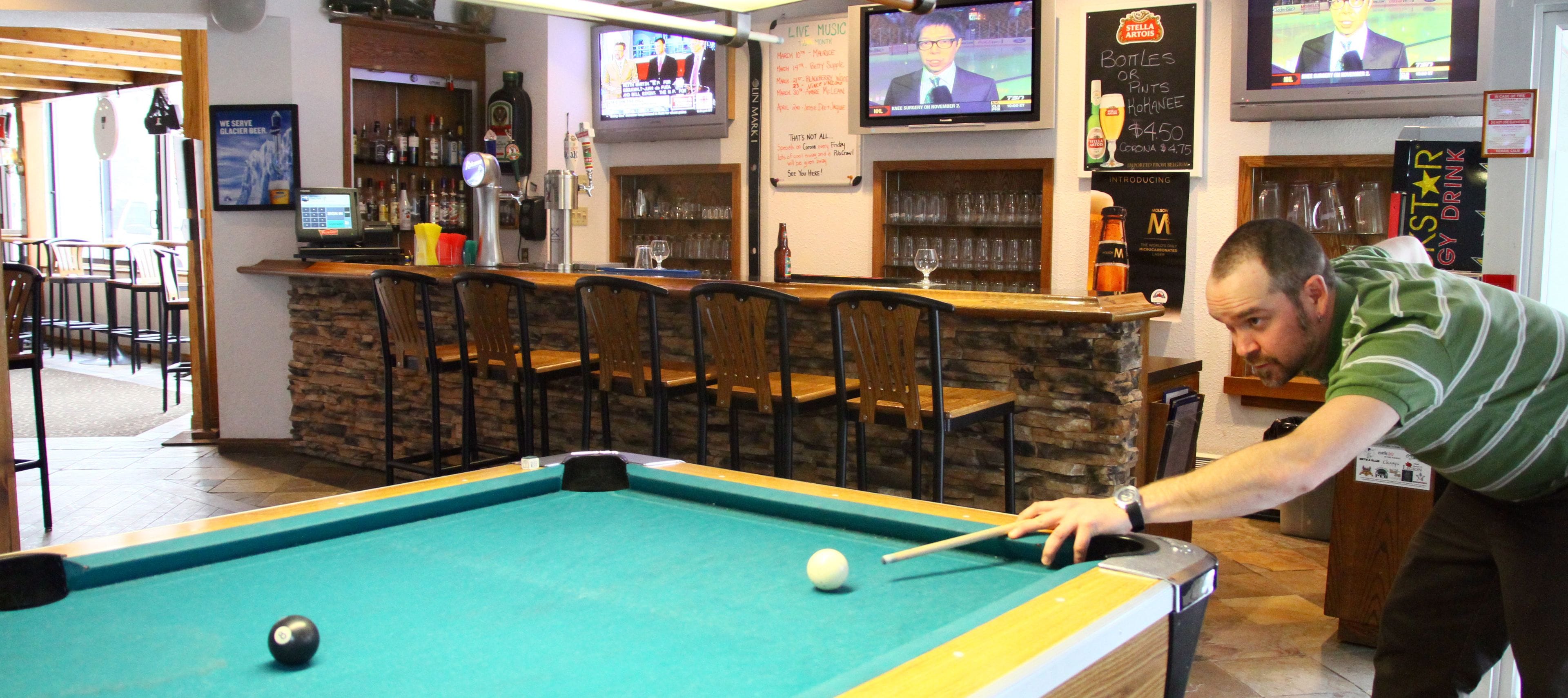 Une table de billard dans un bar, avec plusieurs téléviseurs diffusant des programmes sportifs et des informations.