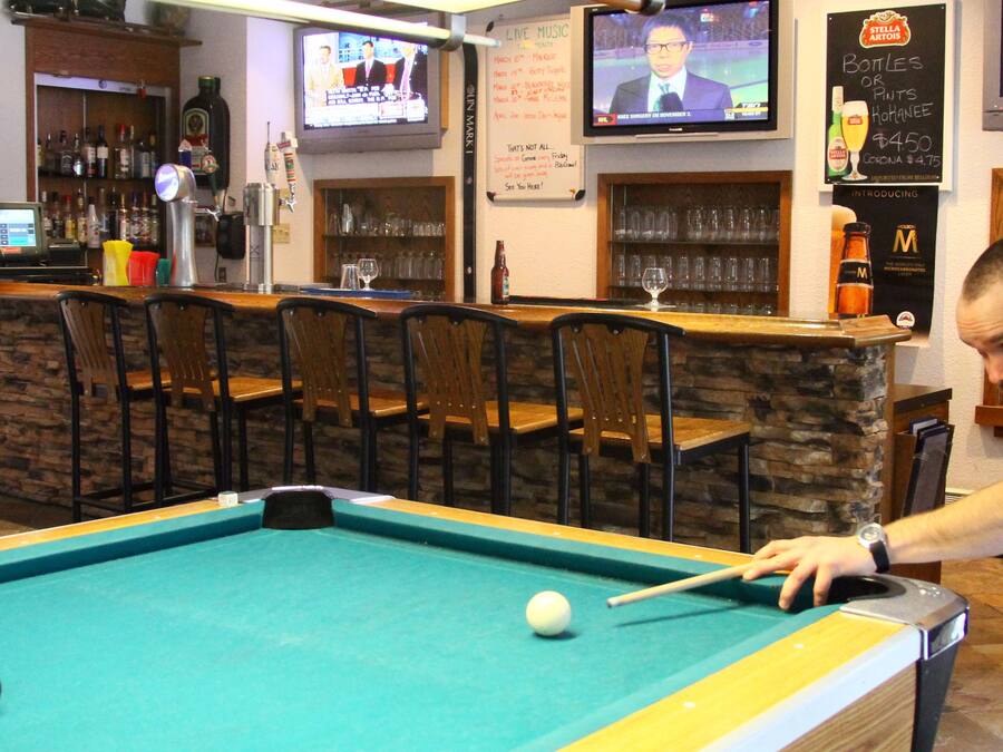 Une table de billard dans un bar, avec plusieurs téléviseurs diffusant des programmes sportifs et des informations.
