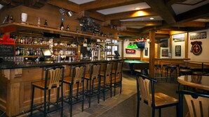 A bar area with wooden bar stools, a pool table, and a variety of liquor bottles.