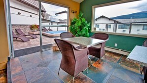 An indoor patio area with wicker furniture, a table, and a view of a pool and buildings outside.