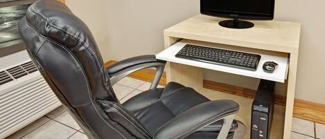 Una silla con respaldo y asiento de cuero, un monitor de computadora, teclado y ratón sobre un escritorio de madera.
