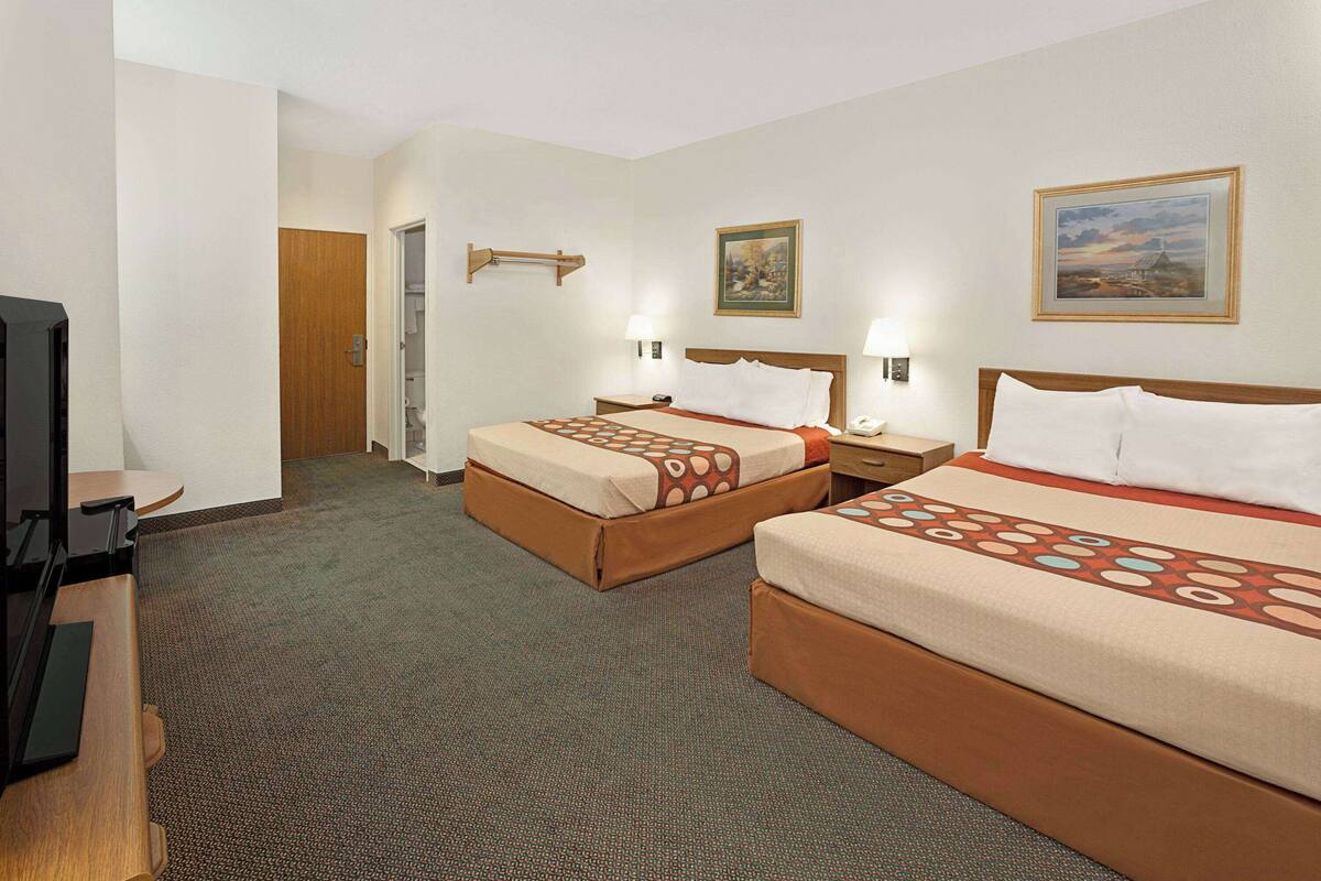 Habitación de hotel con dos camas, un escritorio, un televisor y una puerta que da a un baño.