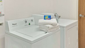 Lavadora Whirlpool de carga frontal con una toalla blanca apilada encima y una caja de detergente.