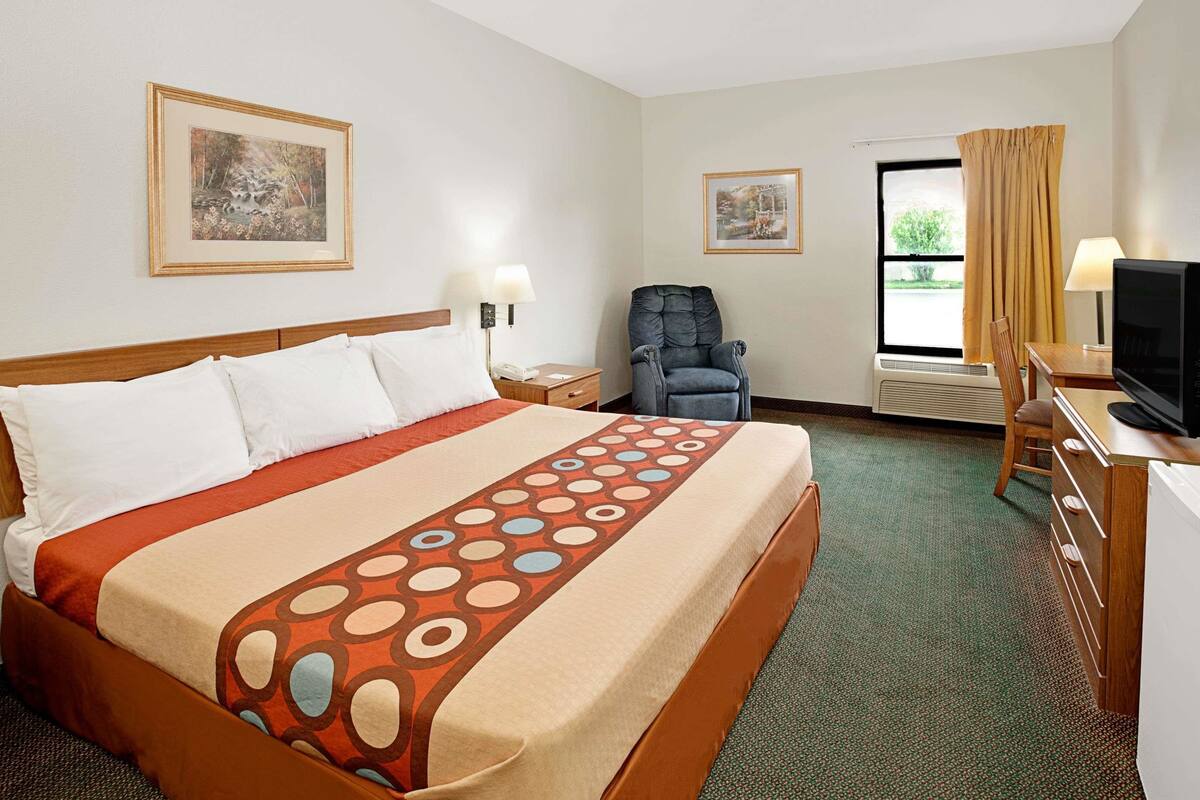 Habitación de hotel con una cama grande, un escritorio con una computadora, una silla y dos cuadros en la pared.