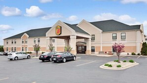 Un hotel con un llamativo letrero de 'Super 8', un estacionamiento con varios coches y una zona ajardinada con un árbol.