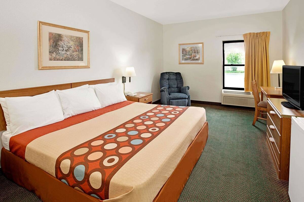 Habitación de hotel con cama, escritorio con televisor, una silla y dos cuadros en la pared.