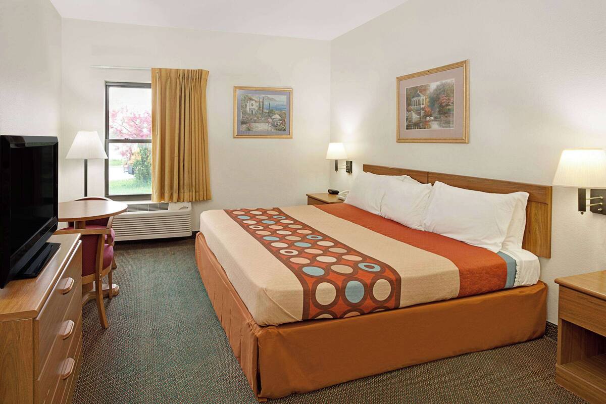 Una habitación de hotel con cama, escritorio, televisor y dos cuadros en la pared.