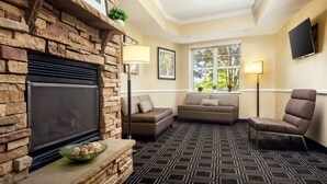A cozy living room with a stone fireplace, two sofas, a chair, and a large window with a view of trees. - TownePlace Suites by Marriott Springfield (Springfield)