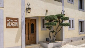 Entrada de hotel com porta de madeira, balcão de recepção e uma placa com a inscrição 'HOTEL ARAGON'.