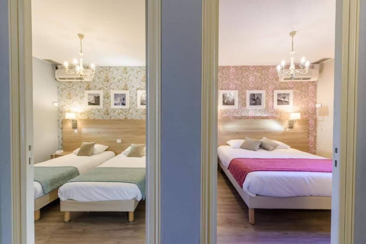 A mirrored view of a hotel room with two beds, a wooden headboard, wall-mounted lamps, and framed pictures.