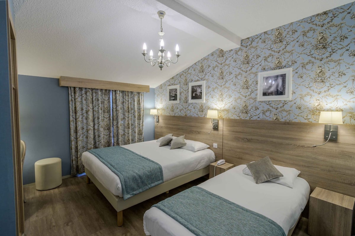 A hotel room with two beds, a chandelier, and a patterned wallpaper.