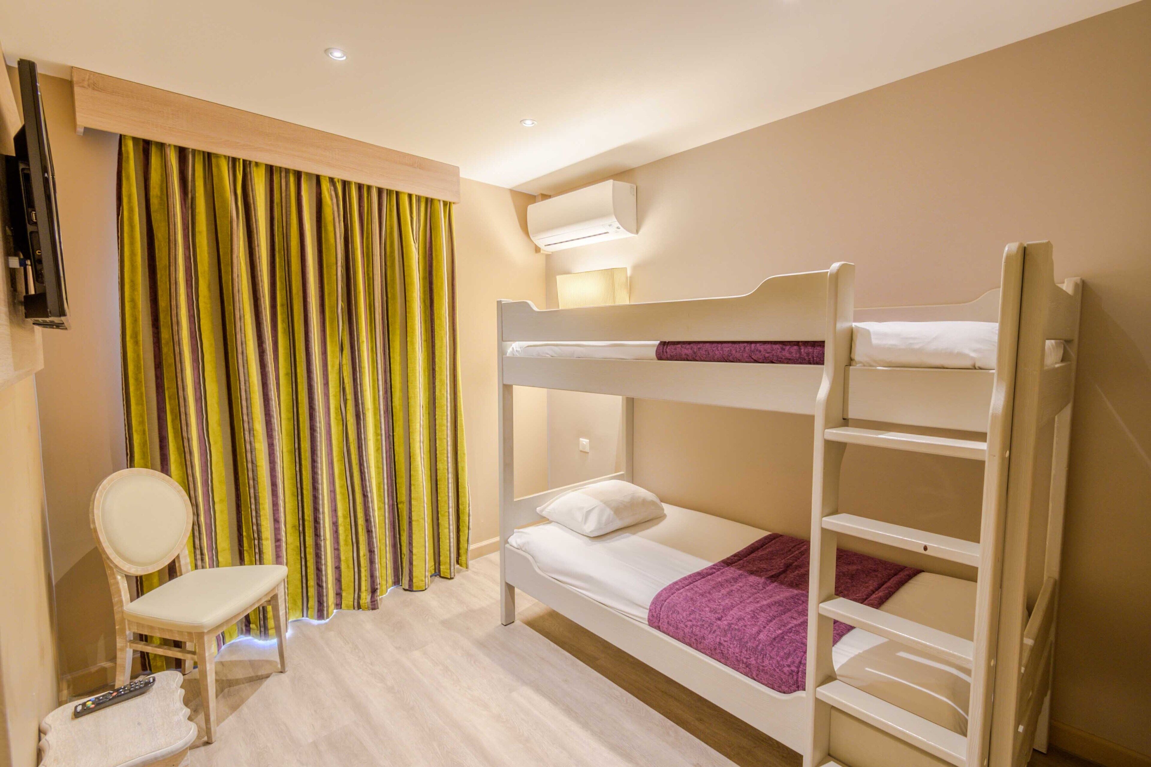A bunk bed room with a small desk and chair, a television, and a window with curtains.