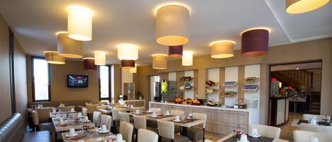 Un restaurante con varias mesas y cabinas, iluminación en el techo, una zona de cocina y una pantalla de televisión en la pared.