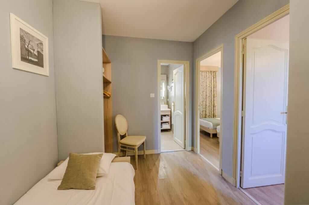 A bedroom with a bed, a chair, a wardrobe, and a door leading to another room.