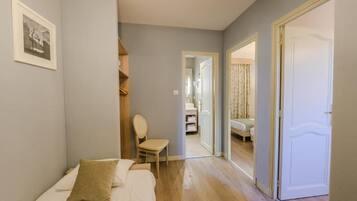 A bedroom with a bed, a chair, a wardrobe, and a door leading to another room.