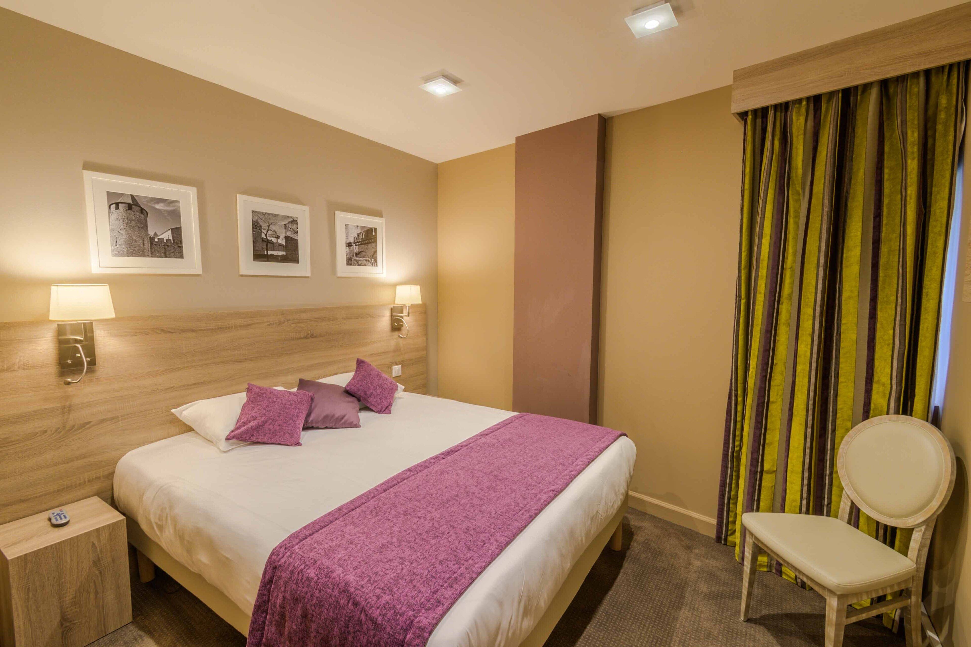 A hotel room with a bed, two bedside lamps, a chair, and three framed pictures on the wall.