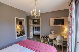 Habitación de hotel con cama, escritorio, silla, televisor y candelabro.