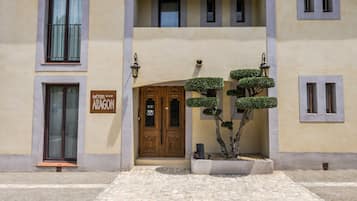 Ein Hotel Eingang mit einer Doppeltür, einem Schild mit der Aufschrift "HOTEL ARAGON" und einem kleinen Garten mit geschnittenen Büschen.
