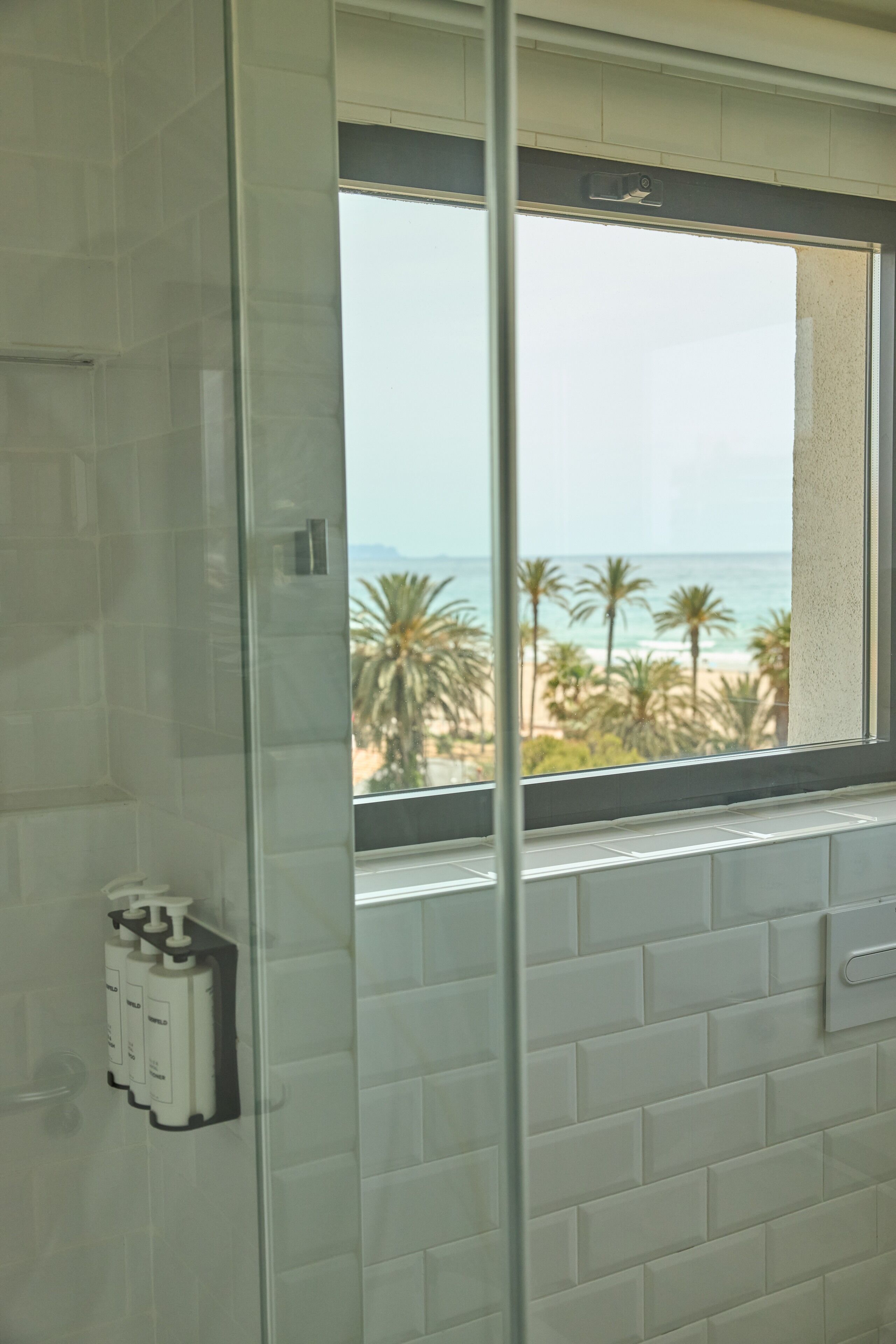 Une salle de bain avec une fenêtre donnant sur la plage, un porte-serviettes et un distributeur de savon.