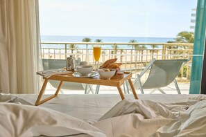 Una cama con un carrito de desayuno en un balcón con vista a la playa.